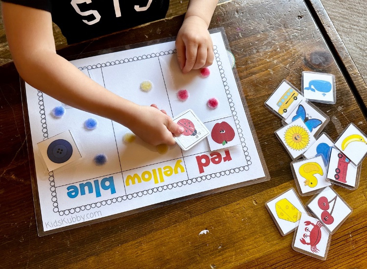 preschooler working on color recognition by sorting colored pictures on a color sorting mat. Use velcro dots to help kids know where to place the pictures in each color column. 