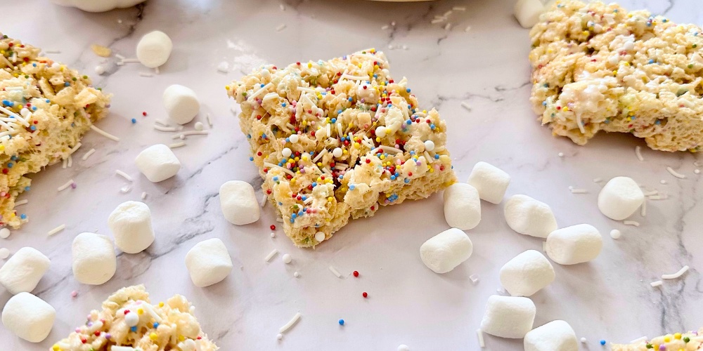 Cake batter rice krispie treats are gooey, delicious, and made with just 5 ingredients including crispy rice cereal, butter, marshmallows, dry cake mix, and rainbow sprinkles for a dash of fun! This easy dessert recipe is perfect for birthdays or party snacks. Make with your favorite brand of funfetti, yellow or white cake mix to take a classic recipe and make it out of this world. My kids love this easy no bake treat! In less than 10 minutes you can make the best Cake Batter Rice Krispie Treats ever!