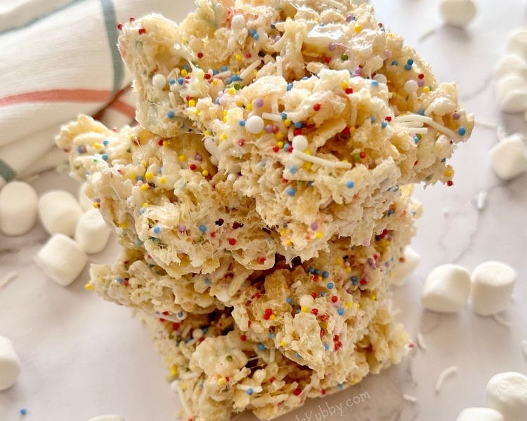 Are you looking for a fun birthday snack for kids? Cake Batter Rice Krispie Treats with rainbow sprinkles are gooey and delicious and kids just gobble them up. Make this easy no bake treat with just a few simple ingredients including crispy rice cereal, butter, marshmallows, dry cake mix, and rainbow sprinkles for a dash of fun! You can take these delectable morsels up a notch by adding a bit of marshmallow creme. Cake batter rice krisipes are fun, yummy, and easy to make in less than 10 minutes.