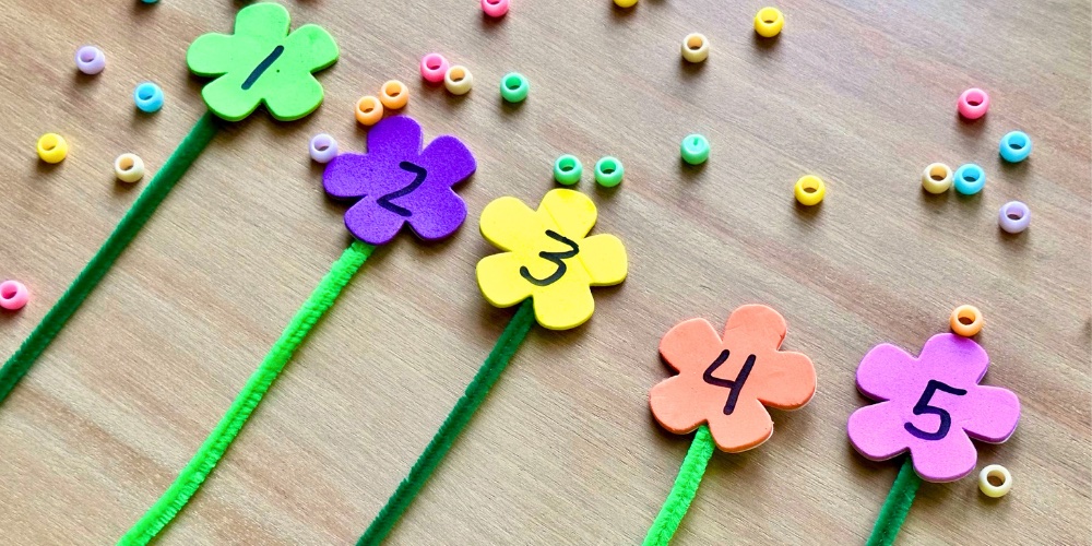 young toddlers can work on fine motor skills by lacing beads on pipe cleaner flowers even if they cannot count the number of beads yet.