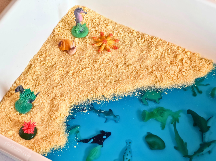 Check out this easy sensory bin idea using Jello! This find the sea animal sensory play idea is perfect for toddlers. Have your toddler use tongs to dig out the sea creatures to help strengthen little hands. Then they can squish, splat, and mix the jello and edible sand for a fun and cheap outdoor activity.