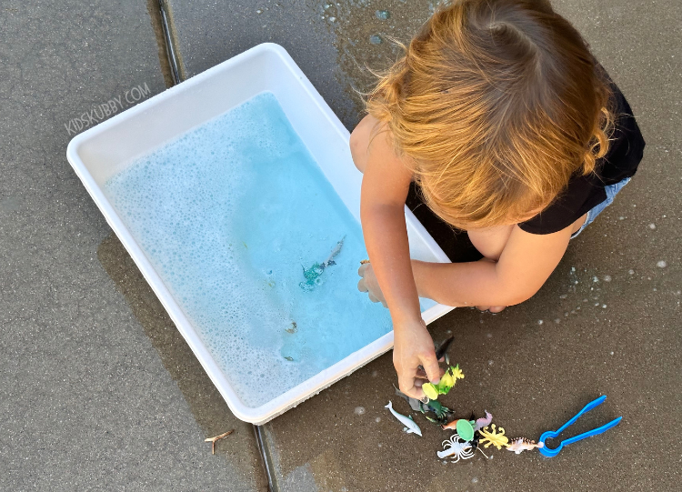 Are you looking for a few new sensory play idea for your kids? well this ocean themed jello sensory bin is fun and cheap to make! all you need is jello, small plastic sea animals and some crushed cheerios. Throw it all together is a plastic container and you have the perfect sensory activity for young kids. This messy outdoor activity is a great way to introduce new textures to sensory sensitive children. Pick up a few boxes of blue jello and make the awesome sensory bin today!