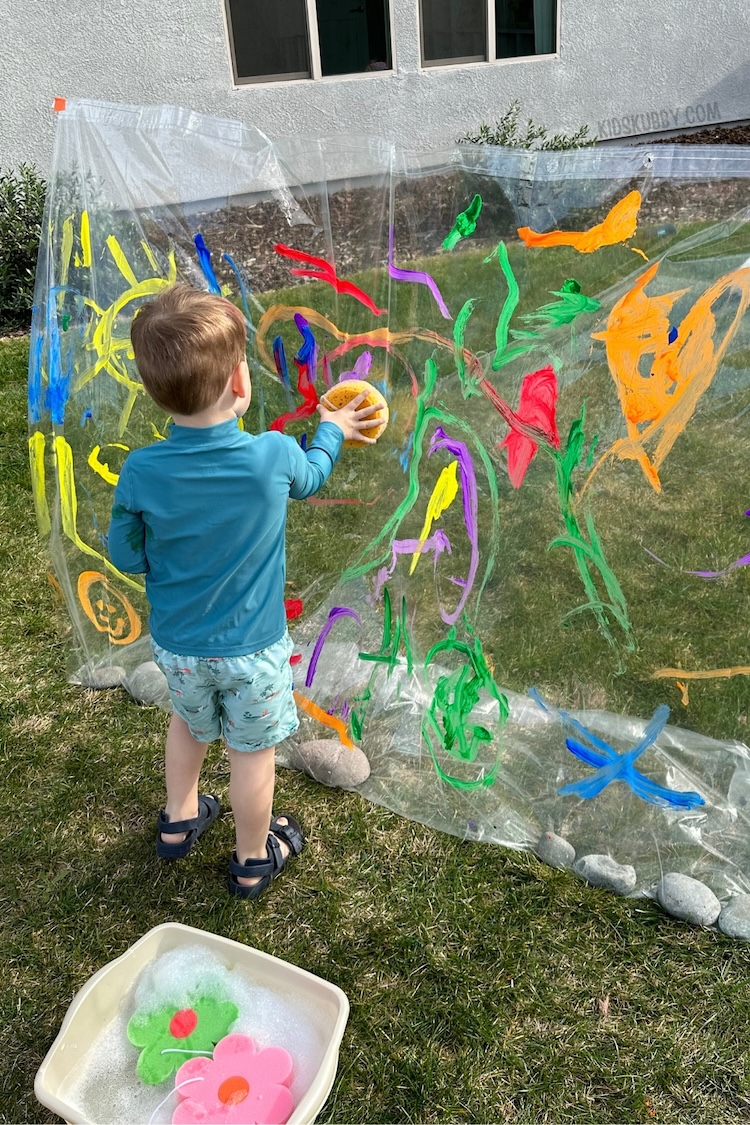 Have you ever tried painting a shower curtain outdoors? This easy to set up summer activity for kids is so fun and budget friendly. All you need is a clear shower curtain, washable paints and some string to create the best ever outdoor activity for kids. 