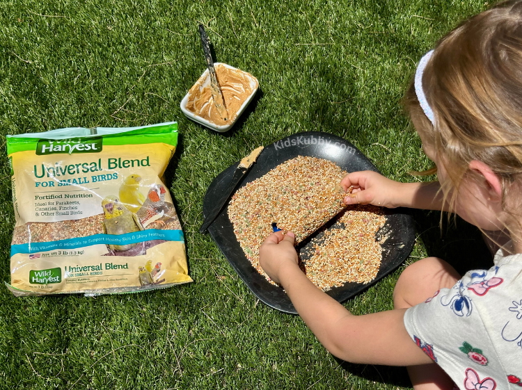 Kids crafting a toilet paper roll bird feeder with peanut butter and birdseed, a fun eco-friendly activity for preschoolers.  
