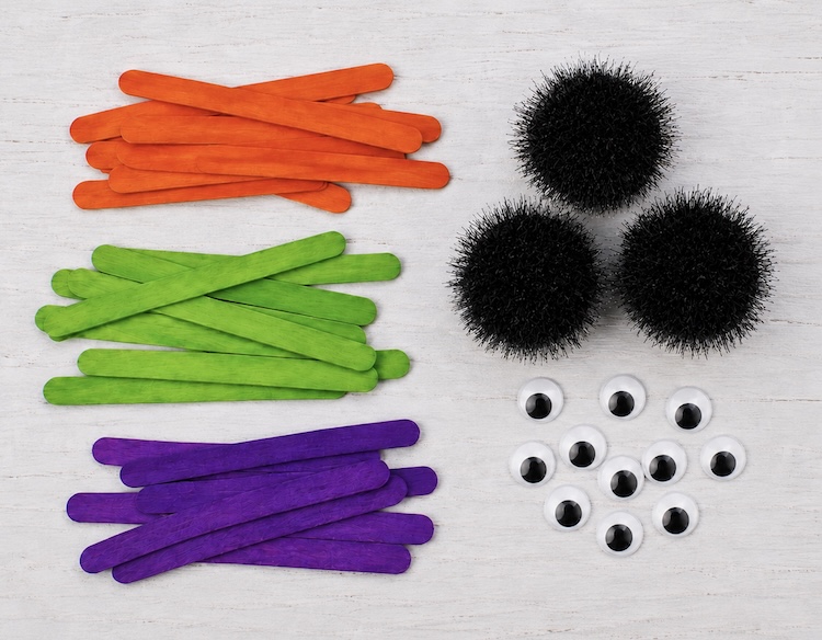 Halloween Popsicle Stick Spiders Craft Supply List: large black pom-poms, colorful popsicle sticks, and large googly eyes. 