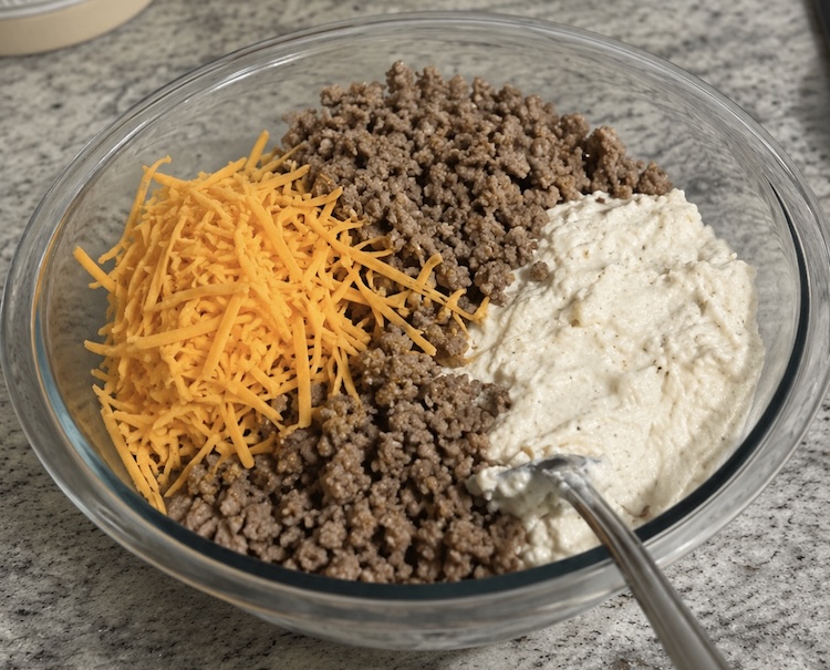 Cooked ground sausage, shredded cheddar cheese, and pancake mix in a bowl ready to be mixed. 