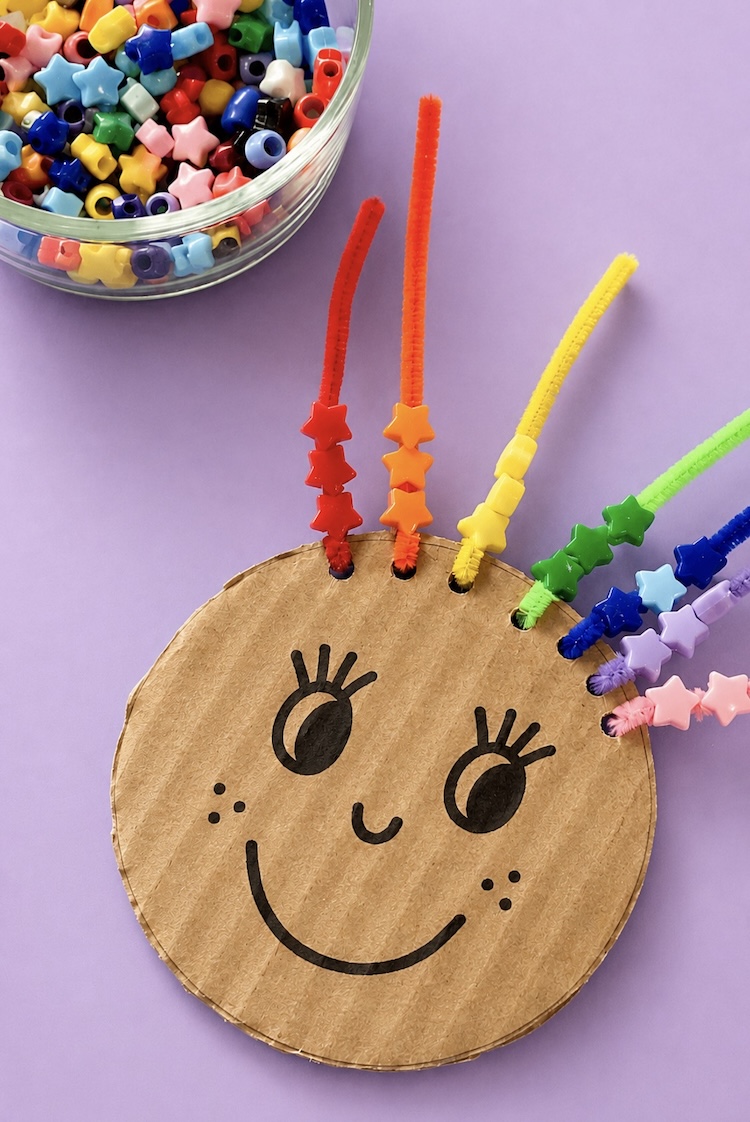 Learning activity for toddlers and preschoolers using cardboard, pony beads, and colorful pipe cleaners. Lacing beads helps with fine motor skills and color recognition for little learners ages 2, 3, and 4.
