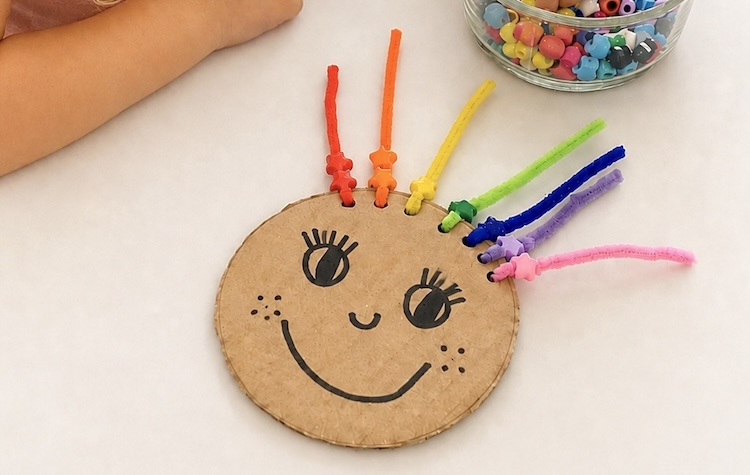 Fun pipe cleaner and bead activity for kids. A learning game placing beads onto rainbow colored hair for toddlers and preschoolers to learn colors and fine motor skills.
