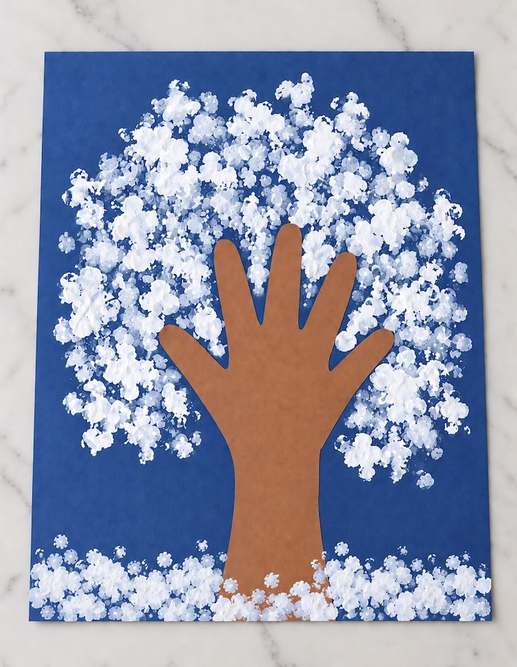 DIY snowy winter tree for Christmas made on construction paper with a brown handprint cut-out for the tree trunk and branches, and snow painted on with q-tips. A fun and easy winter art project for kids.
