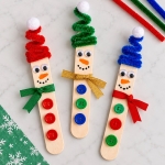 How to make adorable snowmen for Christmas using popsicle sticks and pipe cleaner hats, ribbon scarves, and buttons. A fun and easy craft for kids to make at home. Use them as tree ornaments, magnets, holiday decorations, or trinkets.