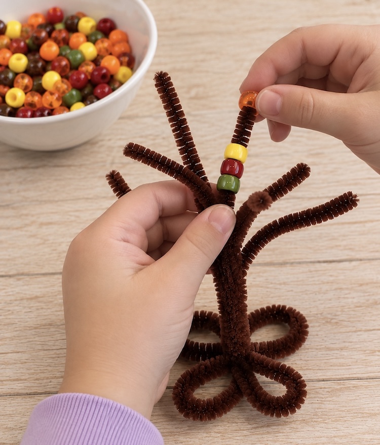 Lacing pony beads onto a pipe cleaner tree.