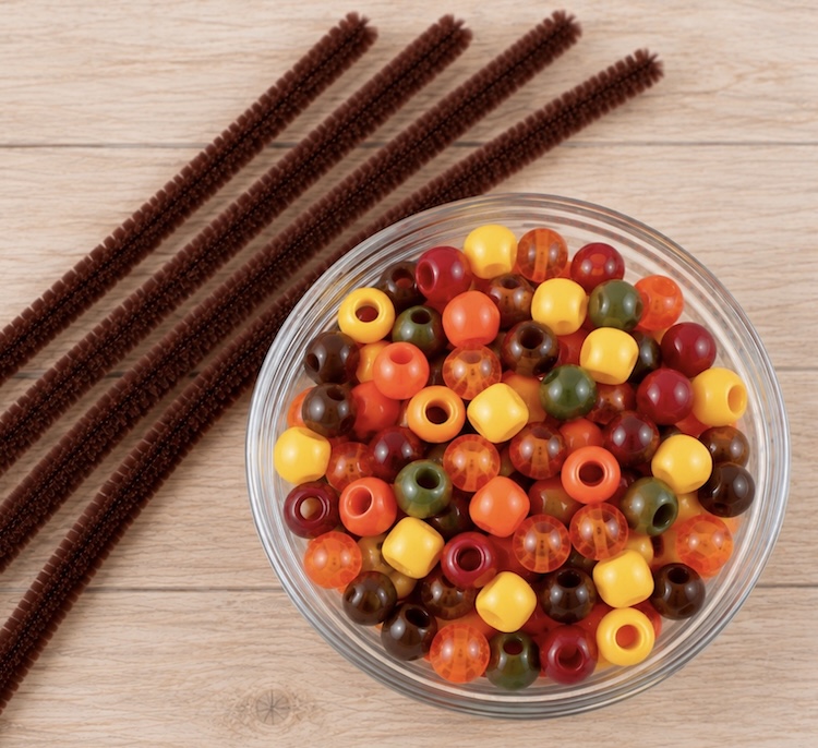 Four brown pipe cleaners and a bowl of fall colored pony beads.