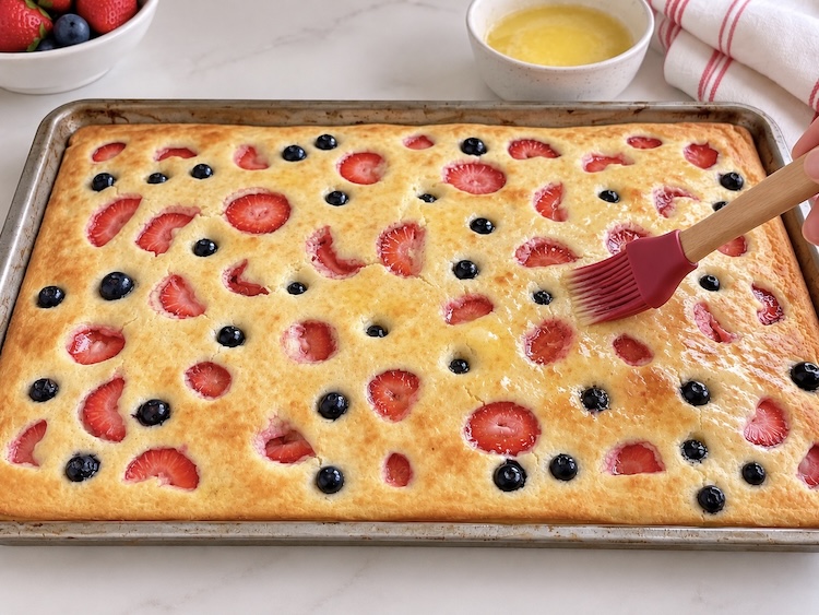 Step 3 of making sheet pan pancakes. Bake in the oven and then immediately brush with melted butter before slicing.