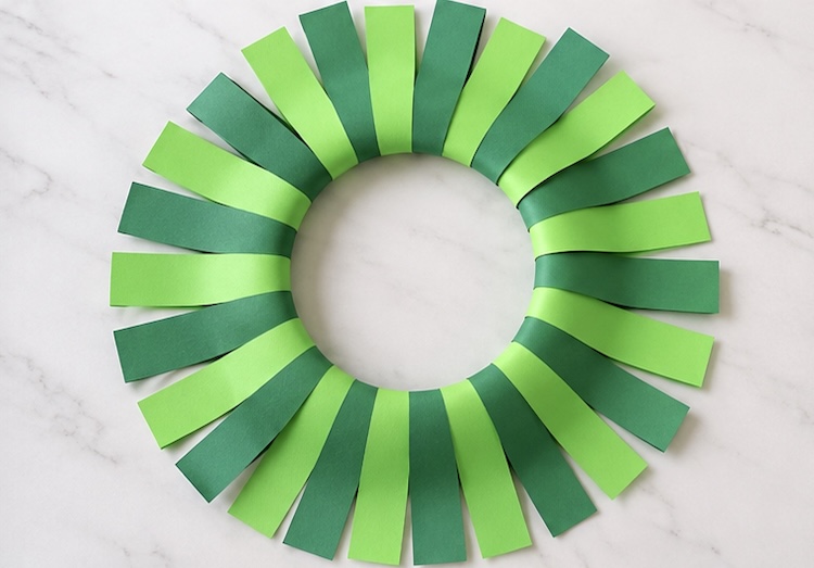 Green strips of paper wrapped around a paper plate and glued together to look like a Christmas wreath.