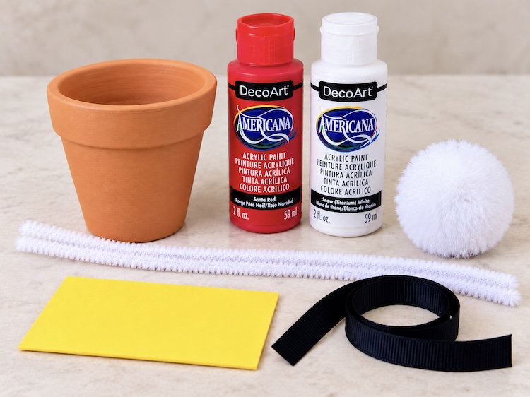 Craft supplies needed for making DIY Santa Hat Christmas Ornaments: mini clay pot, white pipe cleaners, red and white paint, a large white pom-pom, yellow craft foam, and a black ribbon. 