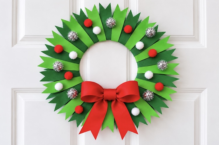 How to make a colorful a festive Christmas wreath using a paper plate, construction paper, pom-poms, and red ribbon.
