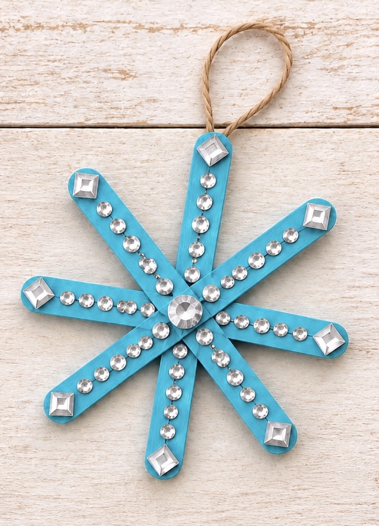 DIY Snowflake Christmas Ornament made with craft sticks and rhinestone stickers. A quick and simple holiday craft for kids to make at home in the winter. These DIY ornaments include a full step by step tutorial and lots of creative ideas on how to decorate them.