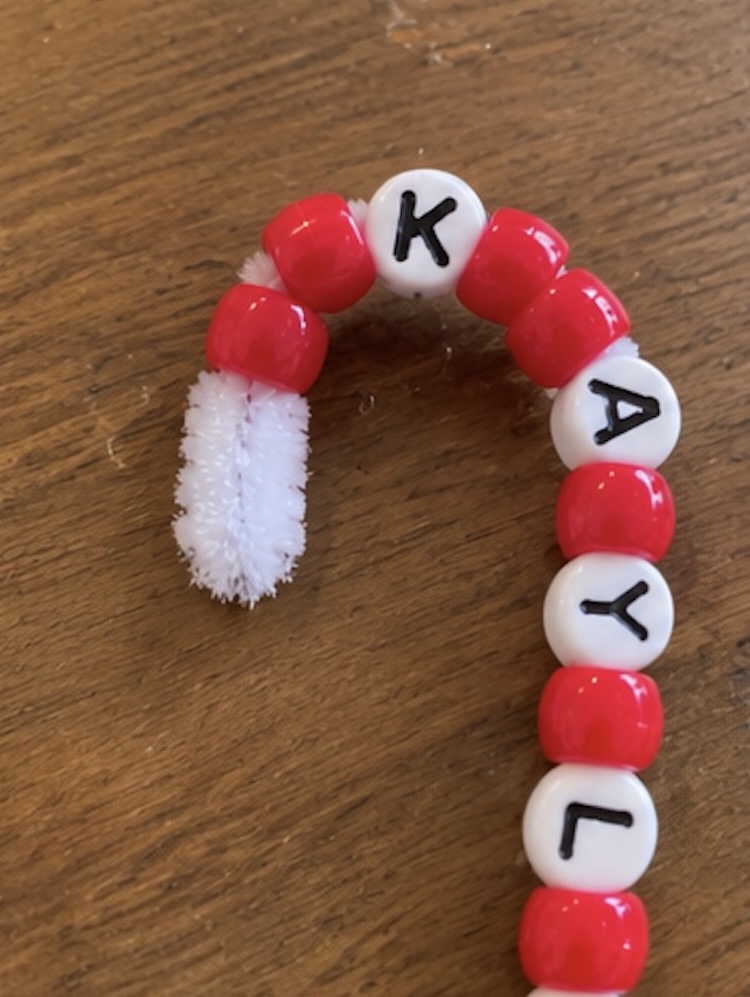 Threading beads onto a pipe cleaner to make DIY candy cane ornaments.