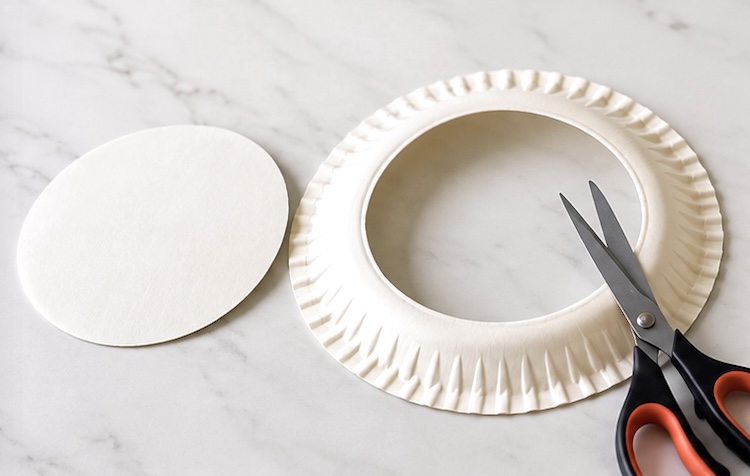 Cutting the center out of a paper plate to make the shape of a wreath.