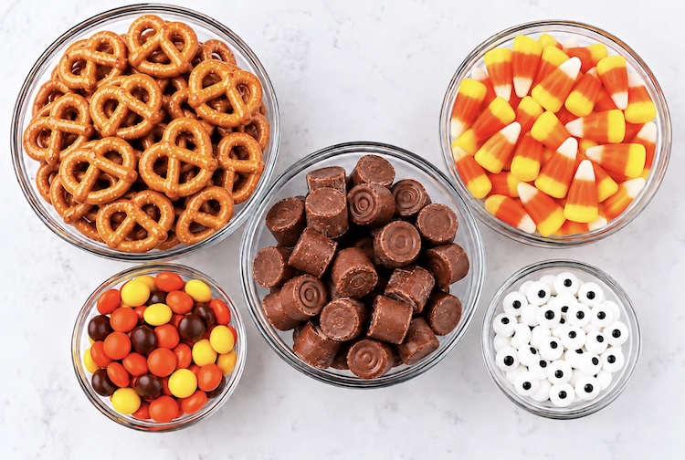Pretzels, Rolos candy, candy corn, Reese's Pieces, and candy eyeballs on a table ready for assemble little turkey treats for Thanksgiving. 