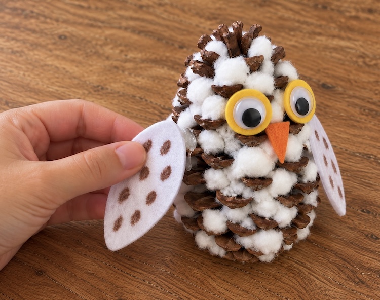 Hot gluing felt wings onto a snowy owl craft made with a simple pinecone and torn pieces of cotton balls. 