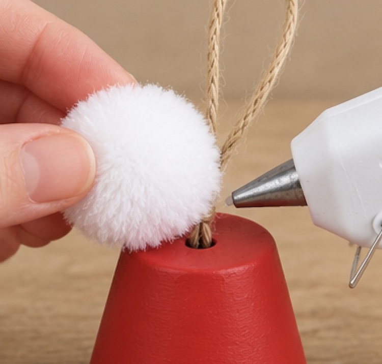 Hot gluing a white Pom Pom on top of a DIY clay pot Santa hat. 