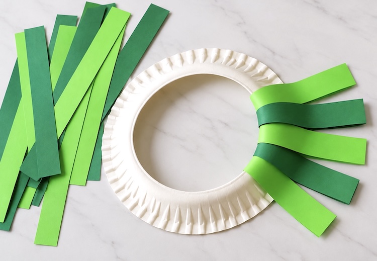 How to make a paper plate wreath with green strips of construction paper. A simple easy craft for Christmas.