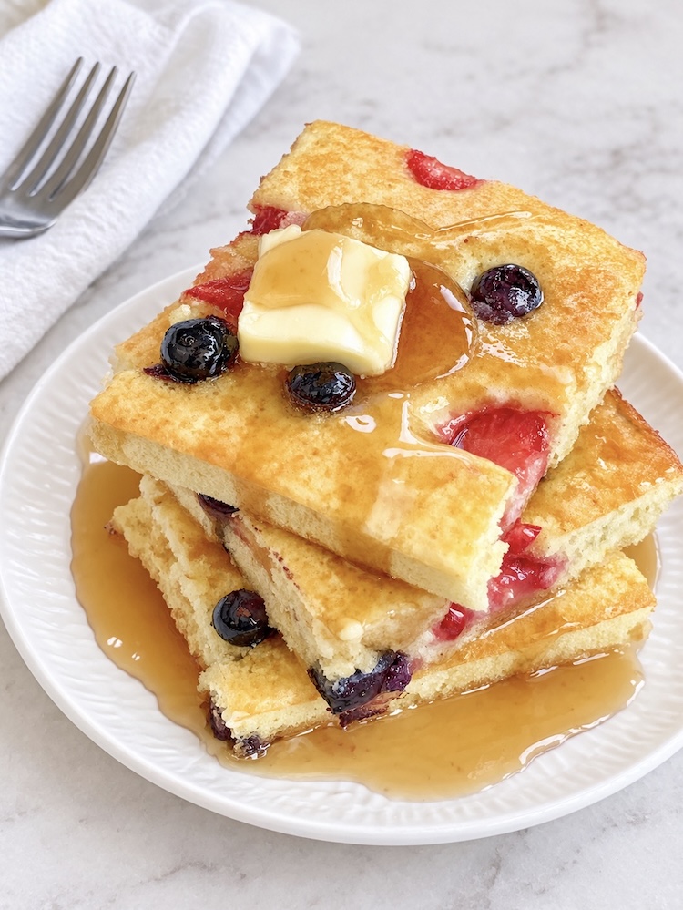 Fluffy pancakes with butter and syrup that have been made in the oven on a sheet pan then cut into small portions.