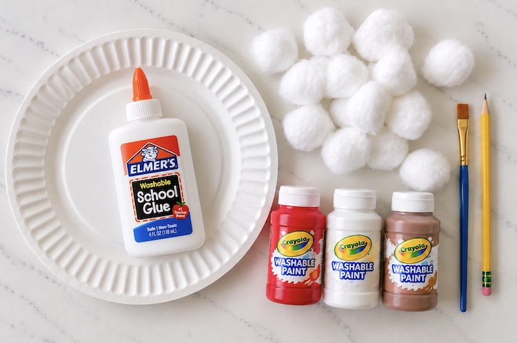 A paper plate, cotton balls, kids washable paint, a paint brush, and a pencil. All supplies needed to make a paper plate santa craft for kids.